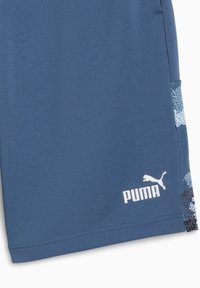 Pantalones cortos deportivos azules hechos de una tela suave, con un patrón sutil en el costado y un logo de Puma blanco cerca del dobladillo.