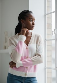 Sweter w paski z miękkiej dzianiny, w kolorach różowym, beżowym i białym; zapięcie na guziki; prążkowane mankiety i dół, o luźnym kroju.