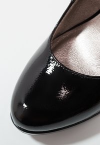Talons aiguille en cuir verni noir avec bout arrondi et finition brillante, dotés d'une doublure intérieure métallique douce et d'une silhouette épurée.