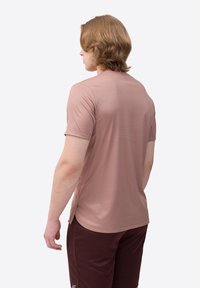 Herren Kurzarmhemd in gedämpftem Rosa, mit weicher Textur, slim fit und subtilen Rippmustern, getragen mit dunklen Sportshorts.