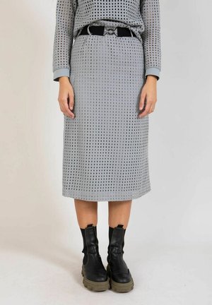 Osoba oblečená v sivej perforovanej sukni a zodpovedajúcom topu s čiernym opaskom, doplnená o masívne čierne členkové topánky na bielom pozadí.