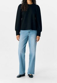 Musta pitkähihaoinen collegepaita, jossa on puffimaiset olkapäät, yhdistettynä vaaleansinisiin suoriin farkkuihin ja mustiin tasapohjaisiin kengiin. Yhteensopiva sileä rakenne.