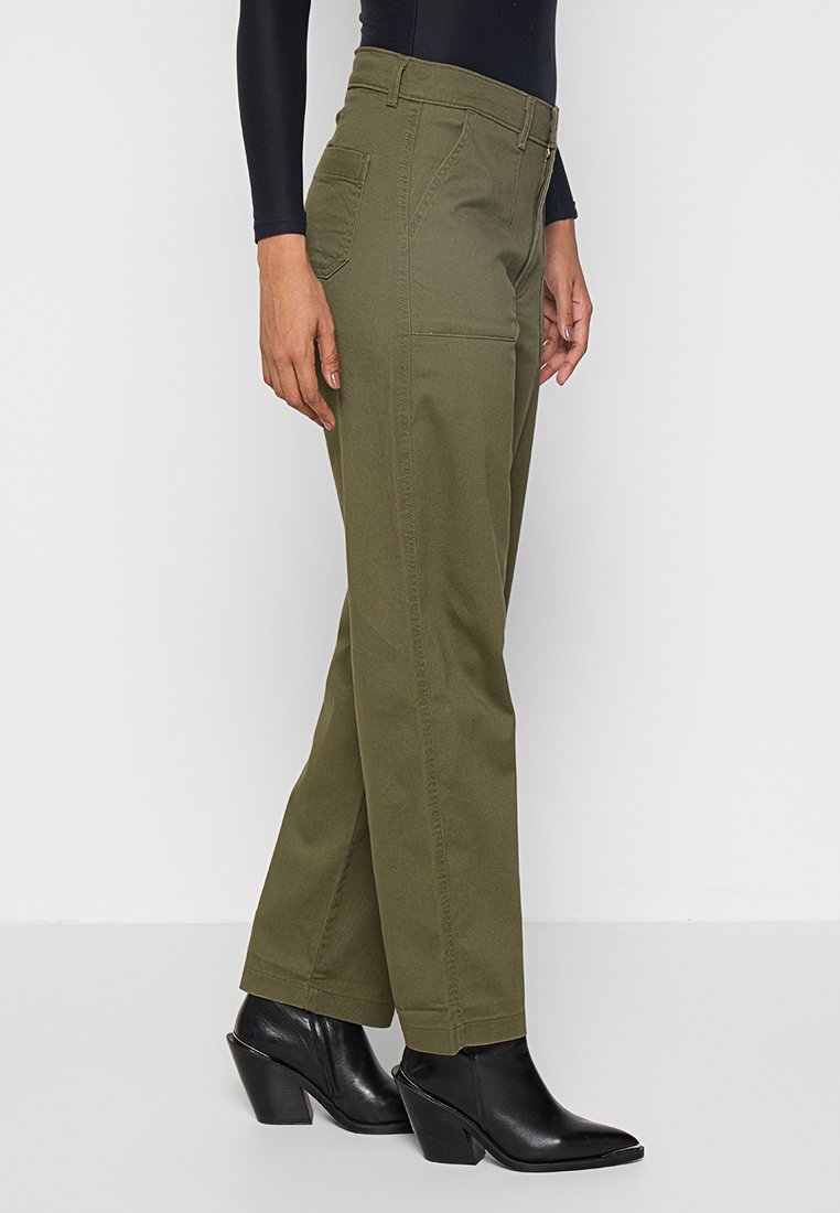 Pantalons larges vert olive en mélange de coton avec une poche latérale, associés à des bottines à talons noires.