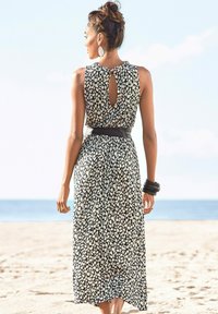 Czarna i biała sukienka w wzory z dekoltem w kształcie łezki, bez rękawów, z czarnym, dopasowanym paskiem w talii oraz zwiewnym materiałem. Tło plażowe.