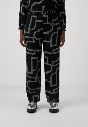 Pantalones negros con un patrón que presenta formas geométricas blancas en contraste, con una cintura elástica, bolsillos laterales y un corte relajado. Combinados con zapatos plateados brillantes.