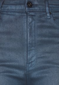 Jeans de mezclilla oscura con corte ajustado, que presentan un cierre frontal de botón, diseño de cinco bolsillos y una textura sutil.