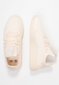 Ett par ljusbeiga stickade sneakers med texturerade sulor, snörning och Adidas Pharrell Williams-logotyp invändigt och på tungan.