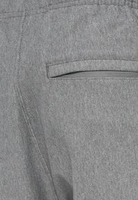 Pilka audinio su smulkiu raštu, matomas galinės kišenės lygus ir tiesus atvartas. Siūlių detalės matomos palei kraštus.