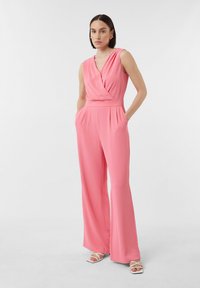Roze mouwloze jumpsuit met een wikkelvoorkant, gestructureerde taille en wijde broekspijpen, voorzien van zijzakken en een soepele stoftextuur.