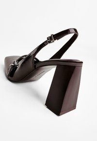 Musta kiiltonahkainen slingback-kengät, joissa on terävä kärki ja paksu neliön muotoinen korko. Koristeltuna metallisoljella.