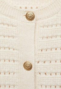 Biały sweter z dzianiny z fakturowanymi paskami, okrągłym dekoltem i złotymi guzikami z przodu. Miękki materiał wełniany.