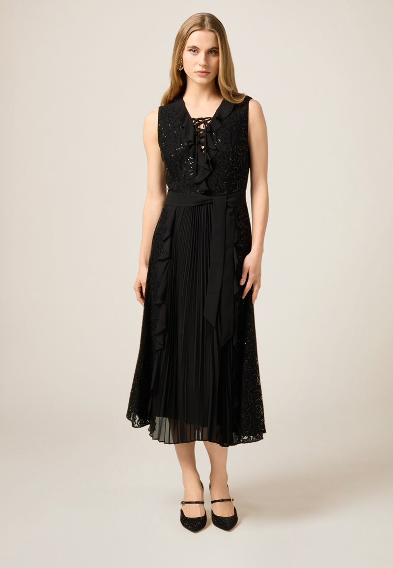 Czarna sukienka z dopasowanym koronkowym gorsetem z cekinami, plisowaną spódnicą, falbanami i wiązaniem w talii. Para czarnych szpilek.