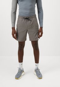 Grå svøm shorts med elastisk talje og snoretræk, iført sammen med en langærmet grå skjorte og grå sneakers.