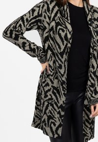 Sweter z dziurawym splotem w czarno-beżowy wzór zebry, z długimi rękawami, luźnym krojem i dwiema przednimi kieszeniami.