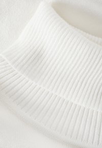 Tessuto a maglia bianco con una trama a coste e colletto. Morbido e liscio, con uno spessore variabile, che mette in evidenza l'artigianato e i dettagli.