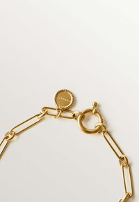 Collar de cadena de oro con eslabones alargados, un cierre circular y una etiqueta redonda con detalles en relieve. Superficie lisa y brillante.