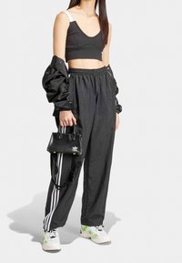 Svart kort topp med vita band, svart glänsande oversize-jacka, svarta träningsbyxor med vita ränder och stora sneakers med gröna accenter.