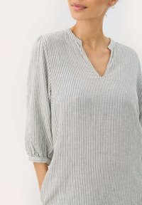 Leichte, gestreifte Bluse mit V-Ausschnitt und 3/4-Ärmeln. Die Farben sind sanftes Grau und Weiß, mit einem entspannten Schnitt und weichem Material.