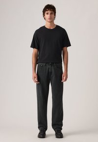 Μαύρο βαμβακερό t-shirt σε συνδυασμό με σκούρο τζιν με ρίγες. Το τζιν έχει ίσια γραμμή και το σύνολο ολοκληρώνεται με μαύρα παπούτσια.