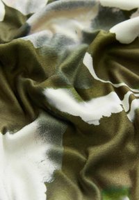Jedwabny szal o miękkiej teksturze z abstrakcyjnym zielono-białym wzorem, prezentujący płynne fałdy i delikatne układanie.