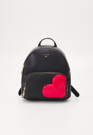 Sac à dos noir Guess avec poche avant présentant un grand patch en forme de cœur rouge brillant embossé du logo "Guess" et des détails de fermeture éclair dorée.