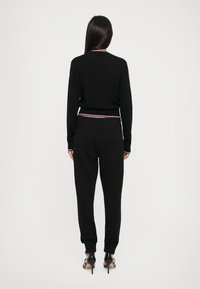 Svart strikkehengete med en kontrasterende ribbestrikket midjebånd og mansjetter. Kombinert med svarte joggebukser, med innsnevrede ben og elastiske mansjetter.