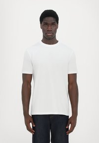 Hvit t-skjorte med rund hals laget av bomull, med korte ermer og en subtil logo på brystet. Kombinert med mørkeblå denimjeans.