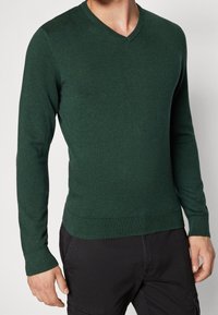 Pull vert à col en V en maille douce et texturée. Manches longues et poignets et ourlet côtelés. Coupe près du corps mettant en valeur une silhouette classique.