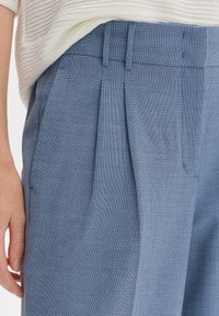 Pantalons texturés bleus avec un devant plissé, présentant une coupe ajustée et une taille lisse. Détails supplémentaires : poches latérales.