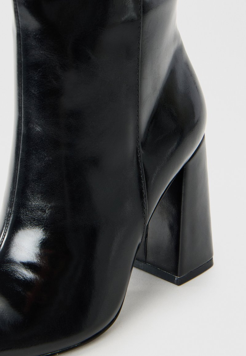 Stivale alla caviglia in pelle nera con una finitura liscia, punta quadrata e tacco geometrico robusto. Il design presenta dettagli di cucitura minimali.