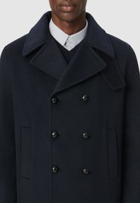 Granatowy wełniany dwurzędowy płaszcz z dużymi czarnymi guzikami, szerokimi klapami i bocznymi kieszeniami. Teksturowany materiał o zbudowanej formie.