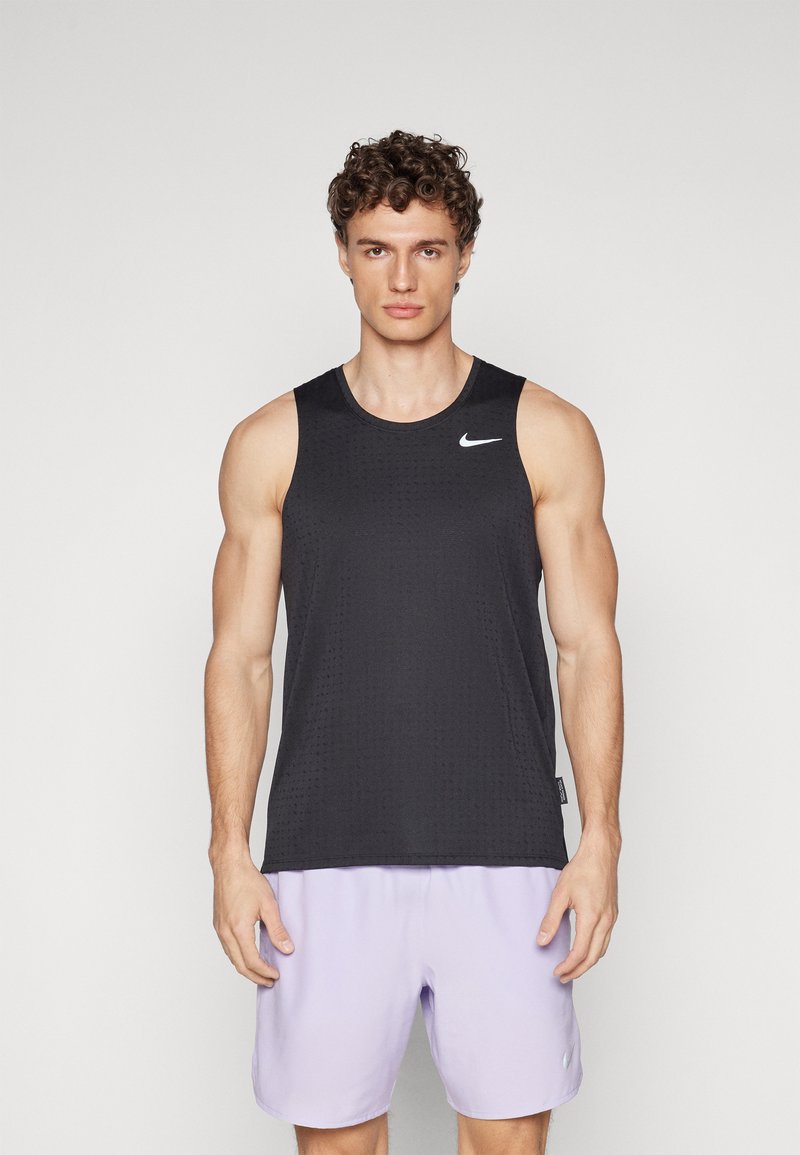Débardeur noir sans manches en tissu texturé avec un logo Nike blanc sur le coin supérieur gauche ; porté avec un short violet clair.