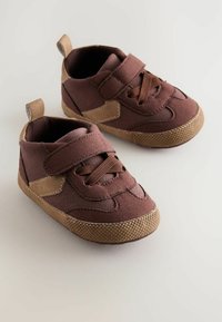 Baskets en tissu marron avec une semelle beige texturée. Équipées d'une bande Velcro et d'un design à lacets. Comprend une languette au talon.