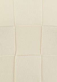 Primo piano di un tessuto in maglia beige con distinti quadrati che mostrano diversi schemi e texture di lavorazione.