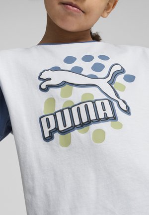 Biała bawełniana koszulka z niebieskimi rękawami, z wyraźnym logo Puma i grafiką wskakującego kota, umieszczona na tle zielonych i niebieskich kropek.
