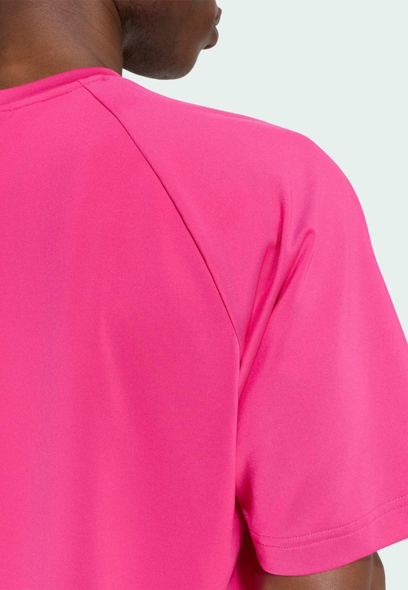 Primer plano de una persona que lleva una camiseta de manga corta de color rosa brillante, mostrando la parte trasera del hombro y el área del cuello.