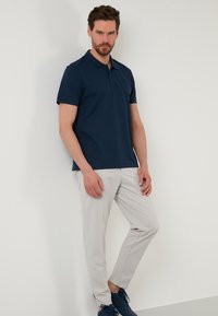 Námořnická modrá polo tričko s krátkým rukávem, texturovaná tkanina, kombinovaná se světle šedými slim-fit kalhotami a námořnickými teniskami. Jednoduchý, moderní design.