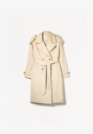 Beige trench coat valmistettu kevyestä kankaasta; kaksirivinen malli, jossa on isot napit, vyötäröhihna ja olkaimen suojukset.