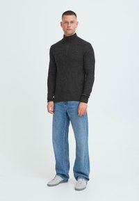 Mørkegrå, tekstureret striktrøje med høj krave, parret med lyseblå, vide jeans og lysfarvede sneakers.