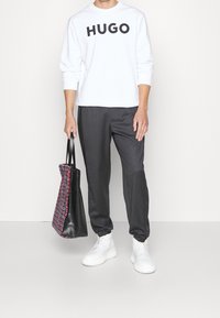 Sudadera blanca con el texto "HUGO" en negro, pantalones de sastre grises y un bolso tote negro con un acento a cuadros en rojo y negro, combinados con zapatillas blancas.