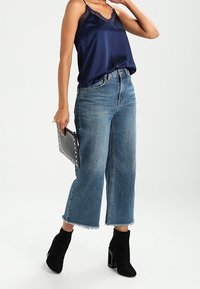 Marinblå satinlinne med spetsdetaljer, ihop med högmidjade, korta blå jeans. Svarta ankelboots och en nitar clutch fulländar looken.