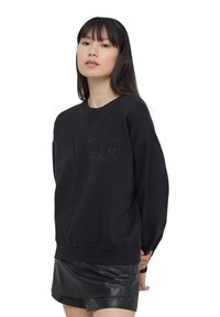 Felpa nera con lettering in rilievo "AMOUR", scollo rotondo, maniche lunghe e vestibilità rilassata, abbinata a una mini gonna in pelle nera.