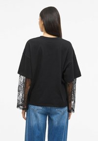 Svart kortermet T-skjorte med blonder lange ermer, med en avslappet passform og rund hals, kombinert med lyseblå vide jeans.