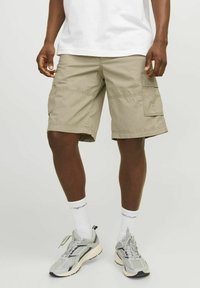Shorts cargo kaki avec plusieurs poches latérales, des détails cousus et une coupe ample, associés à des chaussures de sport grises et blanches ainsi qu'à des chaussettes.