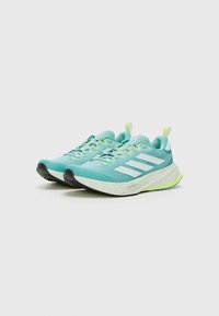 Zapatillas de correr azul claro con acentos en gris y blanco, parte superior de malla, suela negra y una entresuela moteada. Los cordones y las lengüetas del talón son de color amarillo-verde.
