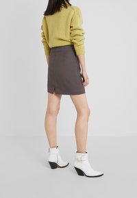 Pull en laine jaune, jupe grise avec fente au dos, et bottes chevilles blanches avec accents noirs sur le talon. Accent sur les textures et les contrastes de couleurs.