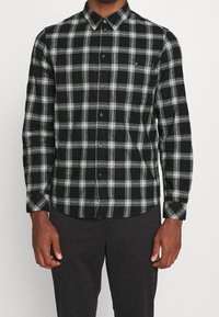 Camicia a quadri nera e grigia con colletto aperto e maniche lunghe, dotata di taschino sul petto e tessuto morbido.