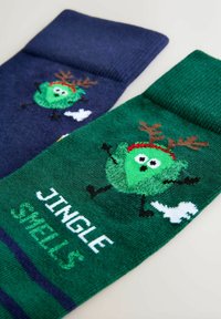 Zeķu pāris; viena tumši zila ar raksturu un ragiem, otra zaļa ar raksturu, tekstu "JINGLE SMELLS" un baltu akcentu. Maiga adīta tekstūra.