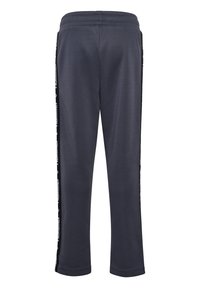 Marineblaue Jogginghose mit elastischem Bund und schwarzen Seitenstreifen mit wiederholendem weißen Grafiktext entlang der Beine.