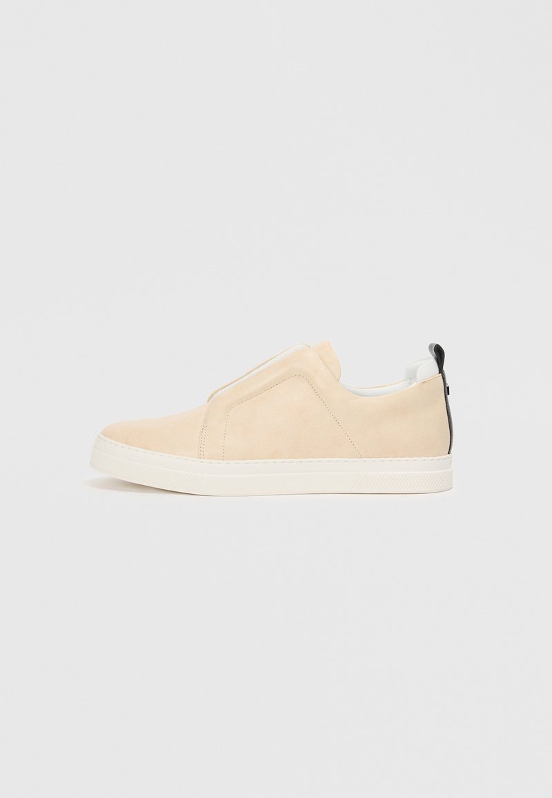 Tenisi slip-on din suede bej, cu o suprafață texturată, talpă din cauciuc albă și un accent negru la călcâi. Design minimalist, fără șireturi.